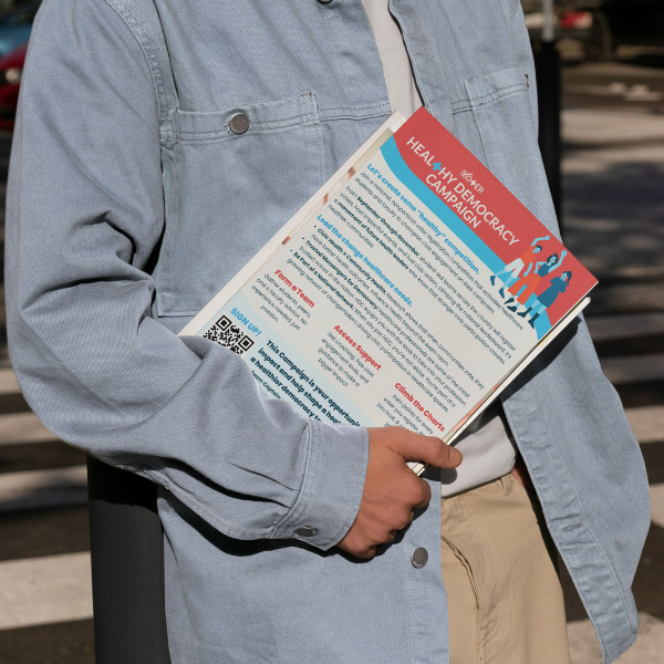Person holding a stack of papers with Vot-ER's Healthy Democracy Campaign one pager on top